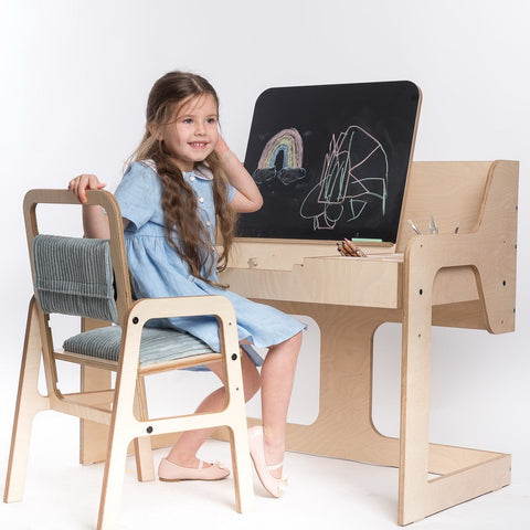 1. Girl in blue dress sitting at Luula mint green Montessori table and chair set, drawing on blackboard in bright room