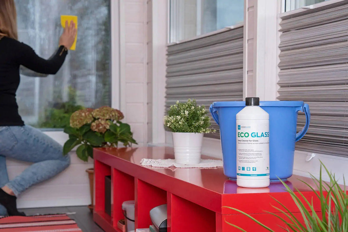 1. Woman cleaning window with GoGoNano EcoGlass cleaner bottle on red table indoors