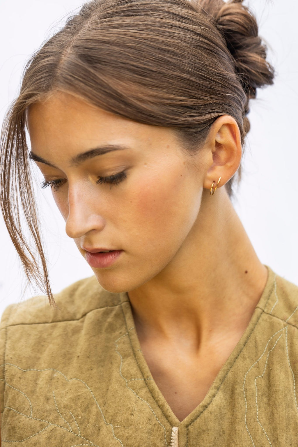 1. Woman looking down wearing Lentsius Sunlit gold-tone earrings, highlighting subtle elegance against light background