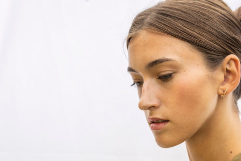 1. Woman wearing Lentsius Sunlit gold-tone earrings, looking to the side with hair in bun against light background