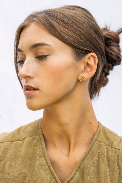 1. Woman wearing Lentsius Sunlit gold-tone earrings with hair in bun, showing side view against light background
