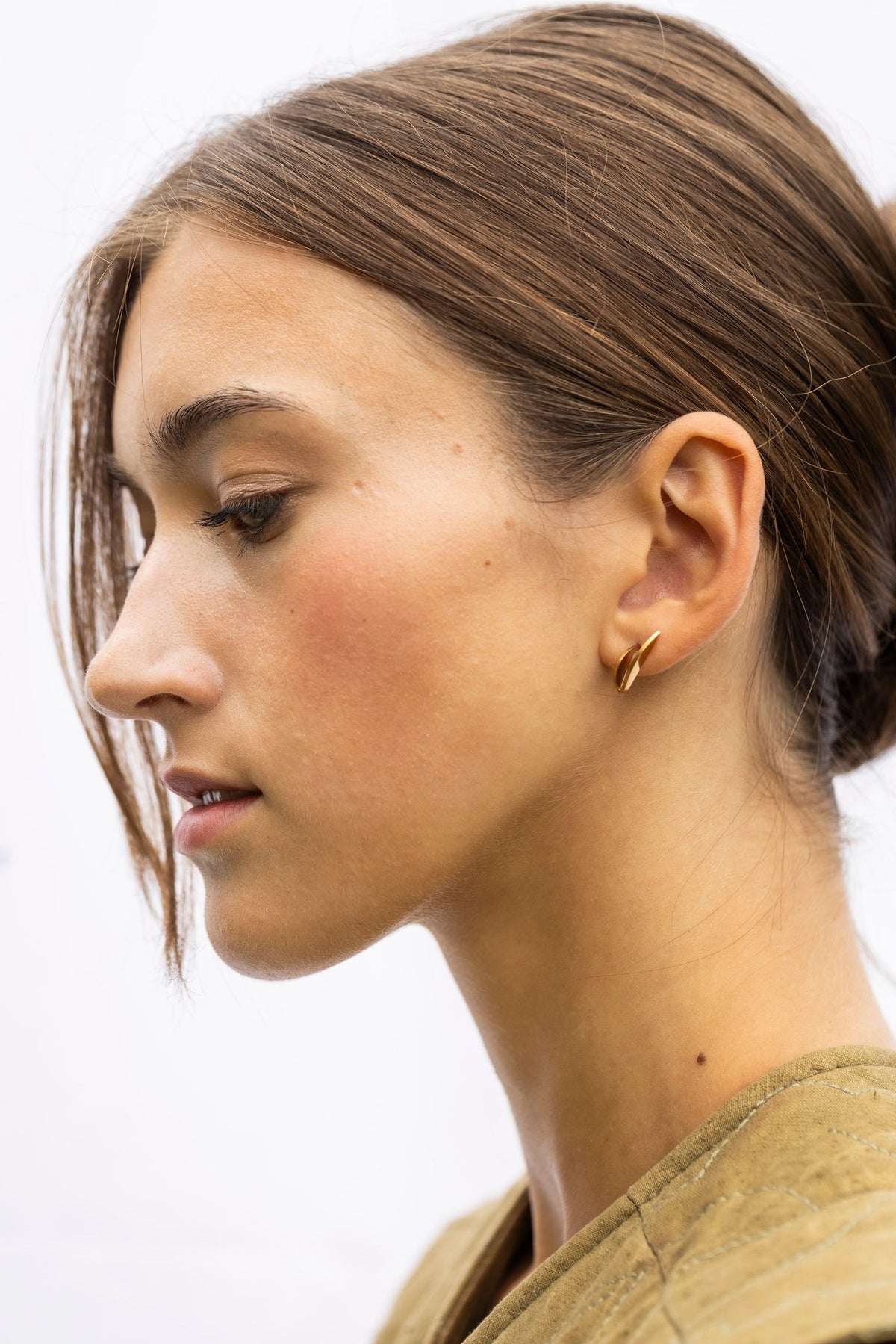 1. Woman in profile wearing Lentsius Sunlit gold-tone earrings, highlighting sleek design against light background