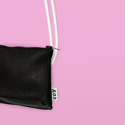 3. Close-up of Daz Studio black leather bum bag with embossed logo on white tag, shown with white strap