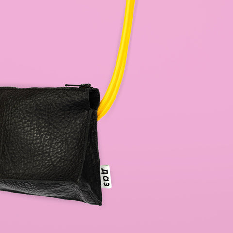 3. Close-up of Daz Studio black leather bum bag showing embossed logo on white tag and yellow strap detail