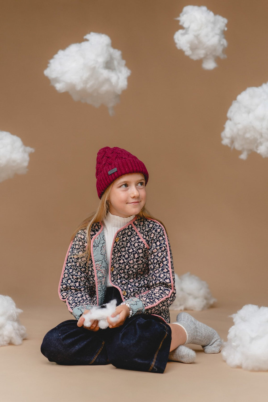 2. Child in Alpaka mulberry cable hat made from 100% baby alpaca, sitting among clouds, highlighting warmth and Nordic design
