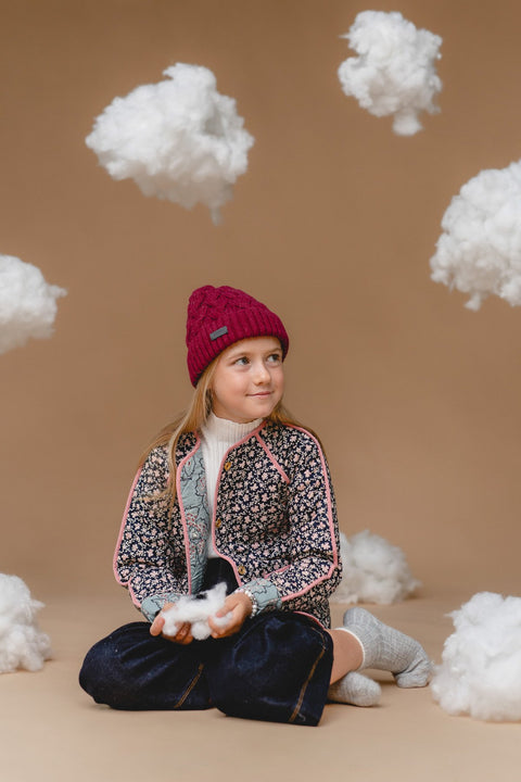 2. Child in Alpaka mulberry cable hat made from 100% baby alpaca, sitting among clouds, highlighting warmth and Nordic design