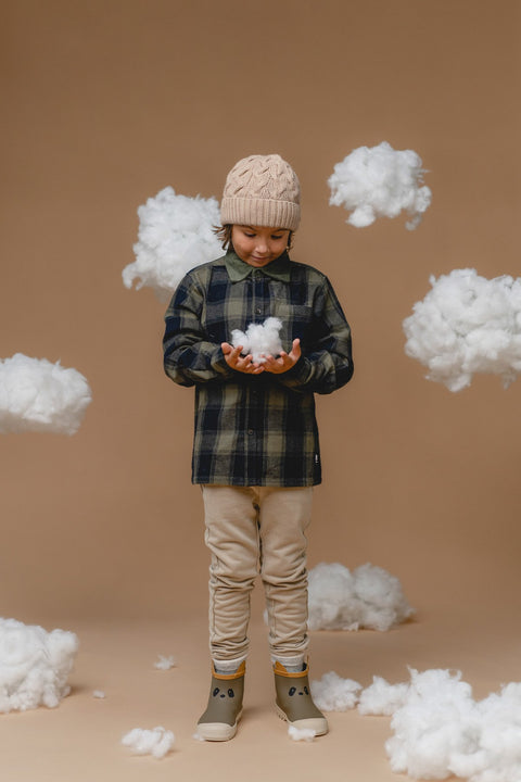 3. Child holding fluffy cloud while wearing Alpaka baby alpaca cable hat in wheat, paired with plaid shirt and beige pants