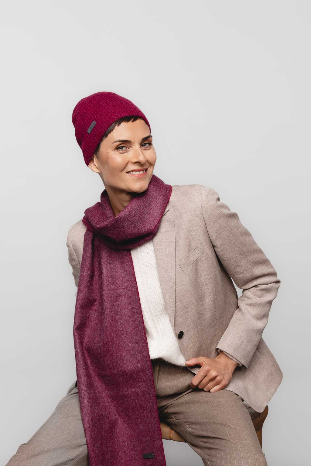 1. Woman wearing mulberry Alpaka baby alpaca wool fisherman's rib beanie with matching scarf, styled with a beige suit