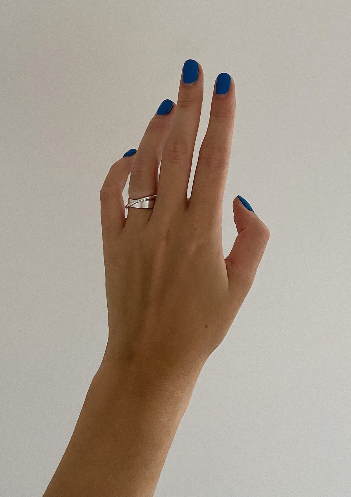 2. Women's hand with blue nails wearing NO MORE Andromeda Ring in sterling silver, shown against a plain background