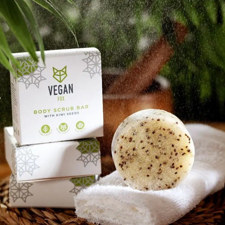 1. Vegan Fox body scrub bar with kiwi seeds on a towel, showcasing packaging and product in a natural setting