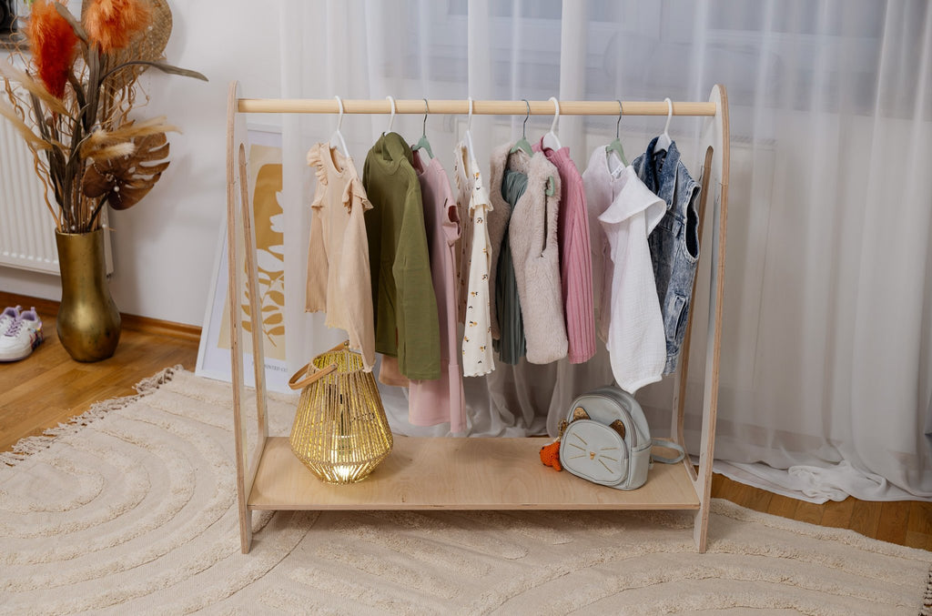 1. Front view of children's white arched clothing rack with hanging clothes and accessories, in a modern room