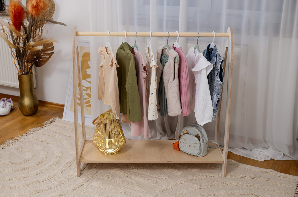 1. Front view of children's white arched clothing rack with hanging clothes and accessories, in a modern room