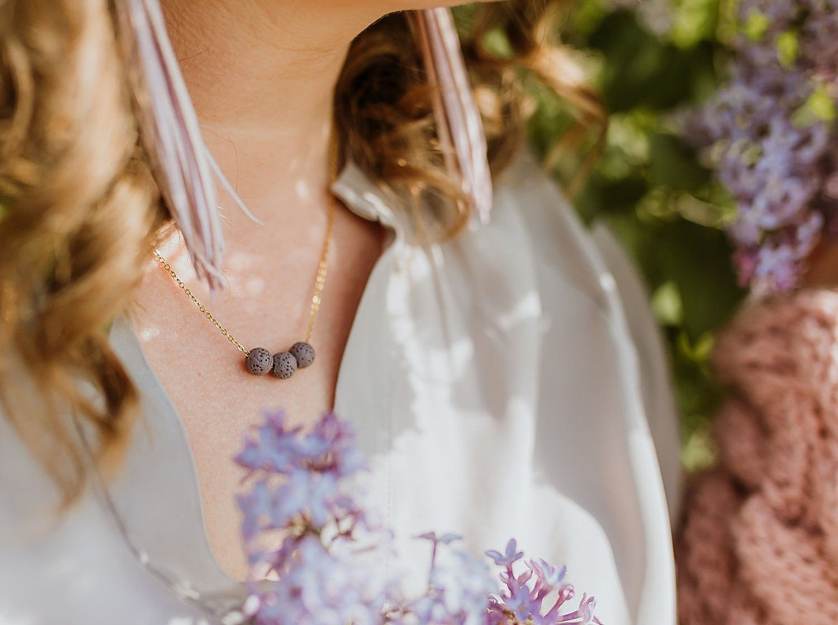 1. Women's aroma diffuser necklace with lava beads on a silver chain, worn outdoors with floral background