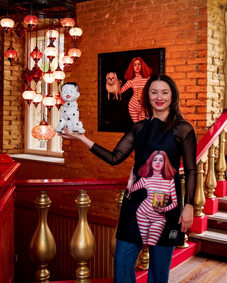 1. Woman wearing Katrin Valgemäe apron with pop art design, holding a spotted dog statue in a warmly lit restaurant