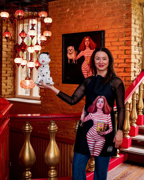 1. Woman wearing Katrin Valgemäe apron with pop art design, holding a spotted dog statue in a warmly lit restaurant