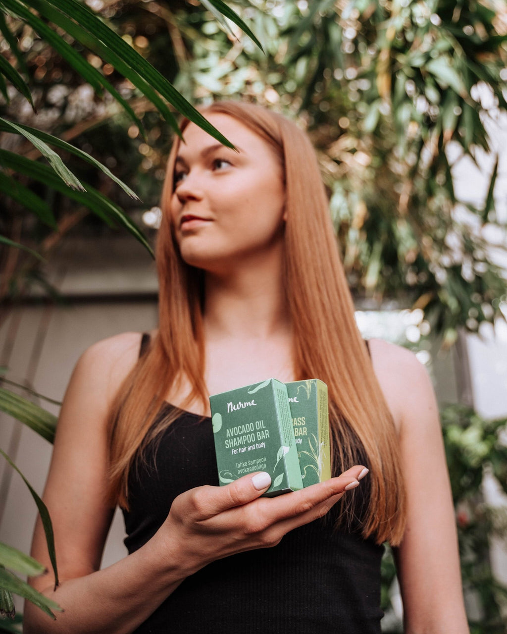 1. Woman holding Nurme avocado oil shampoo bar in a garden setting with lush greenery