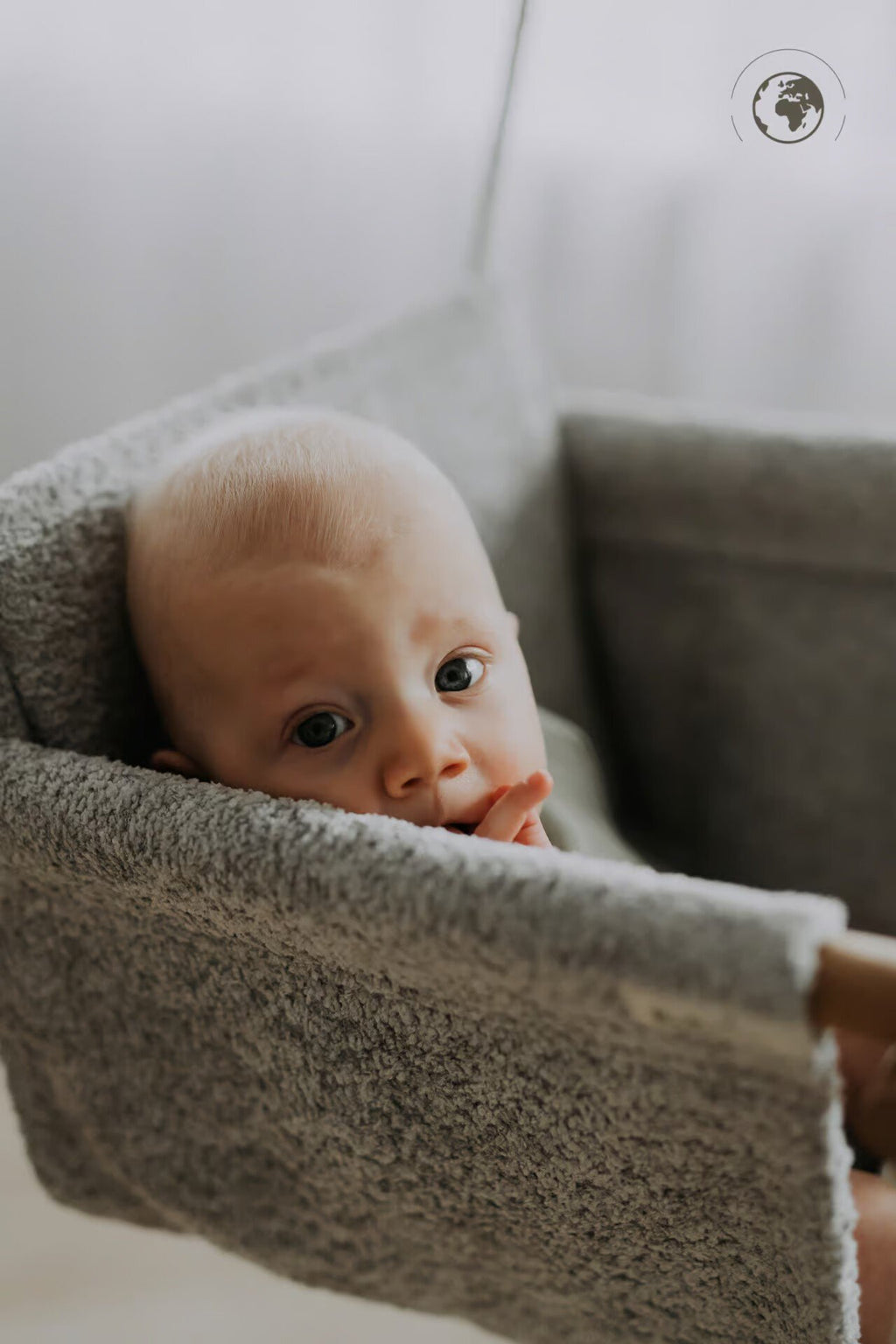 4. Baby resting in grey bouclé fabric baby swing with oak wood poles, looking towards camera indoors