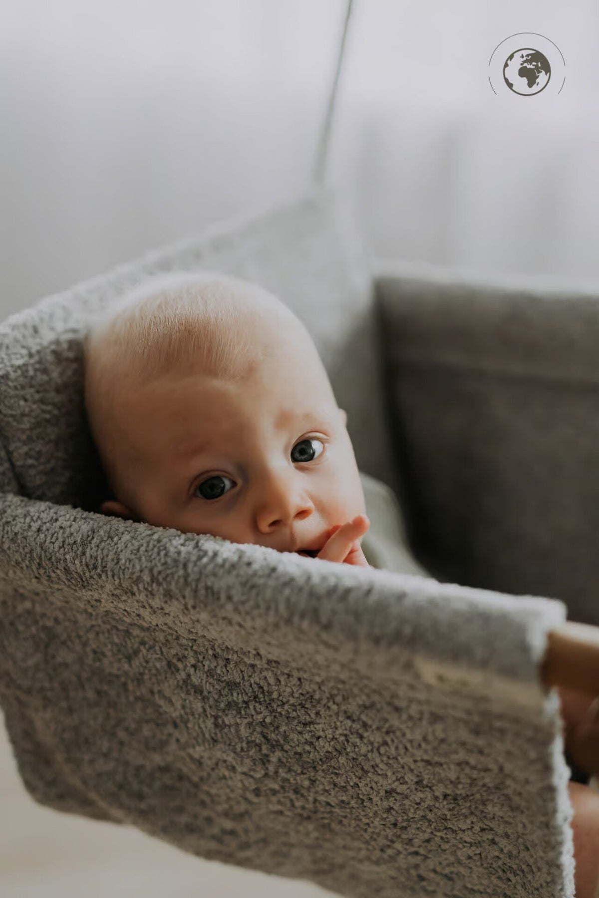 4. Baby resting in grey bouclé fabric baby swing with oak wood poles, looking towards camera indoors