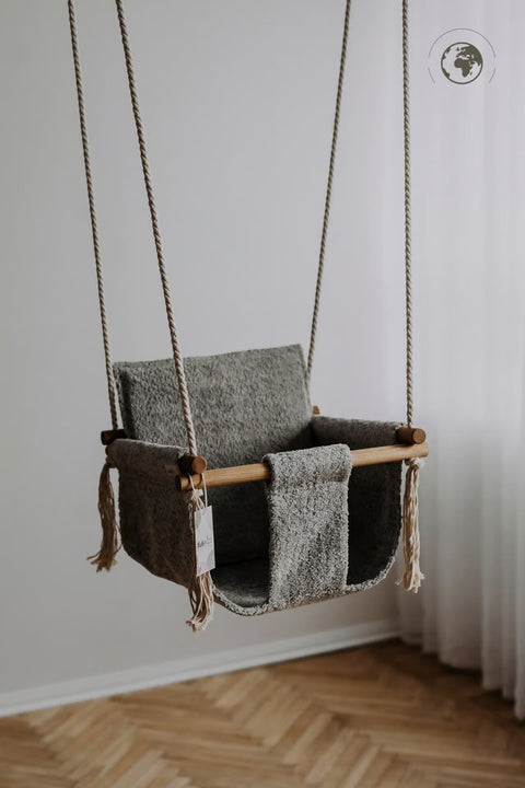 1. Grey bouclé fabric baby swing with oak wood poles hanging in a minimalist room with wooden floor