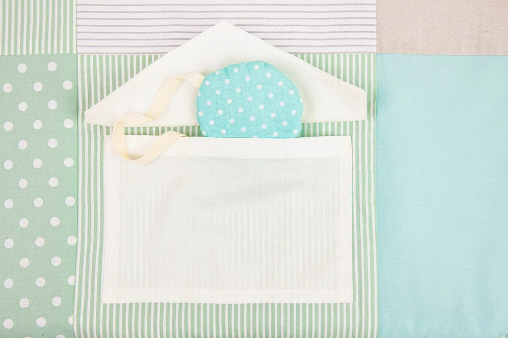 7. Detail of mint green polka dot fabric pocket with attached toy on baby activity mat