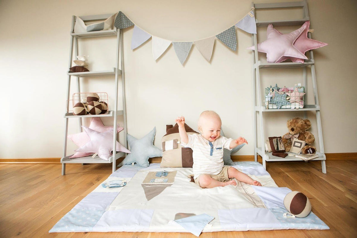 1. Baby sitting on blue activity mat in a nursery setting with toys and shelves