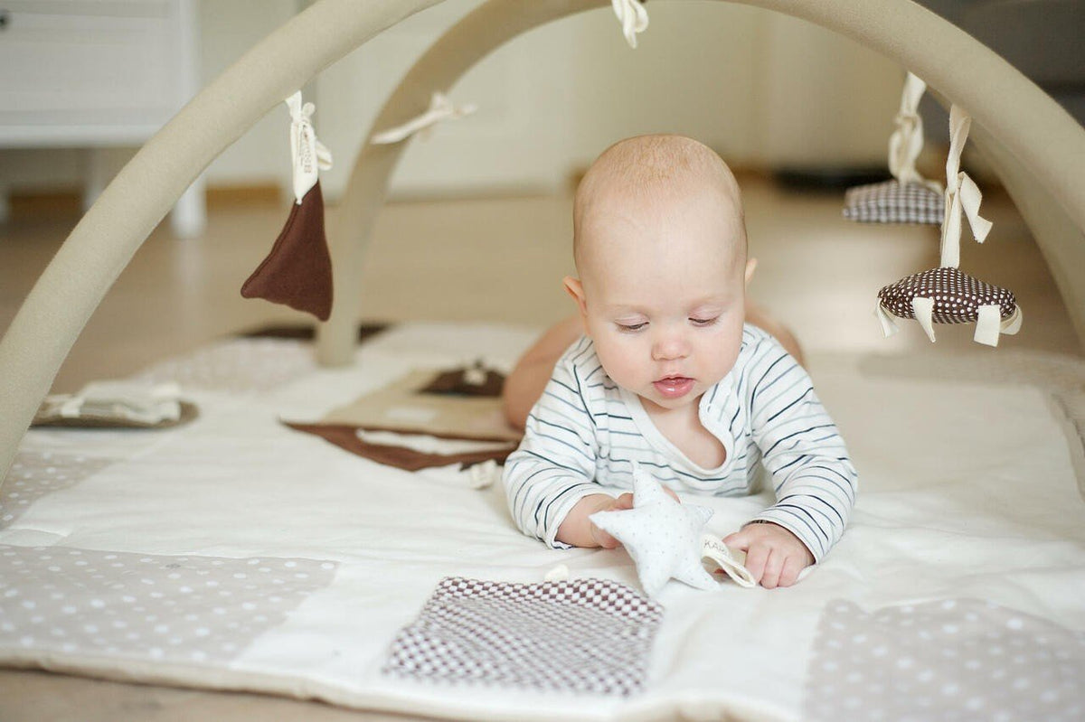 7. Baby on tummy time on brown activity mat with removable arches