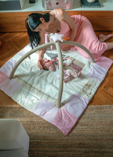 1. Woman in pink dress playing with baby on pink activity mat with arches in living room