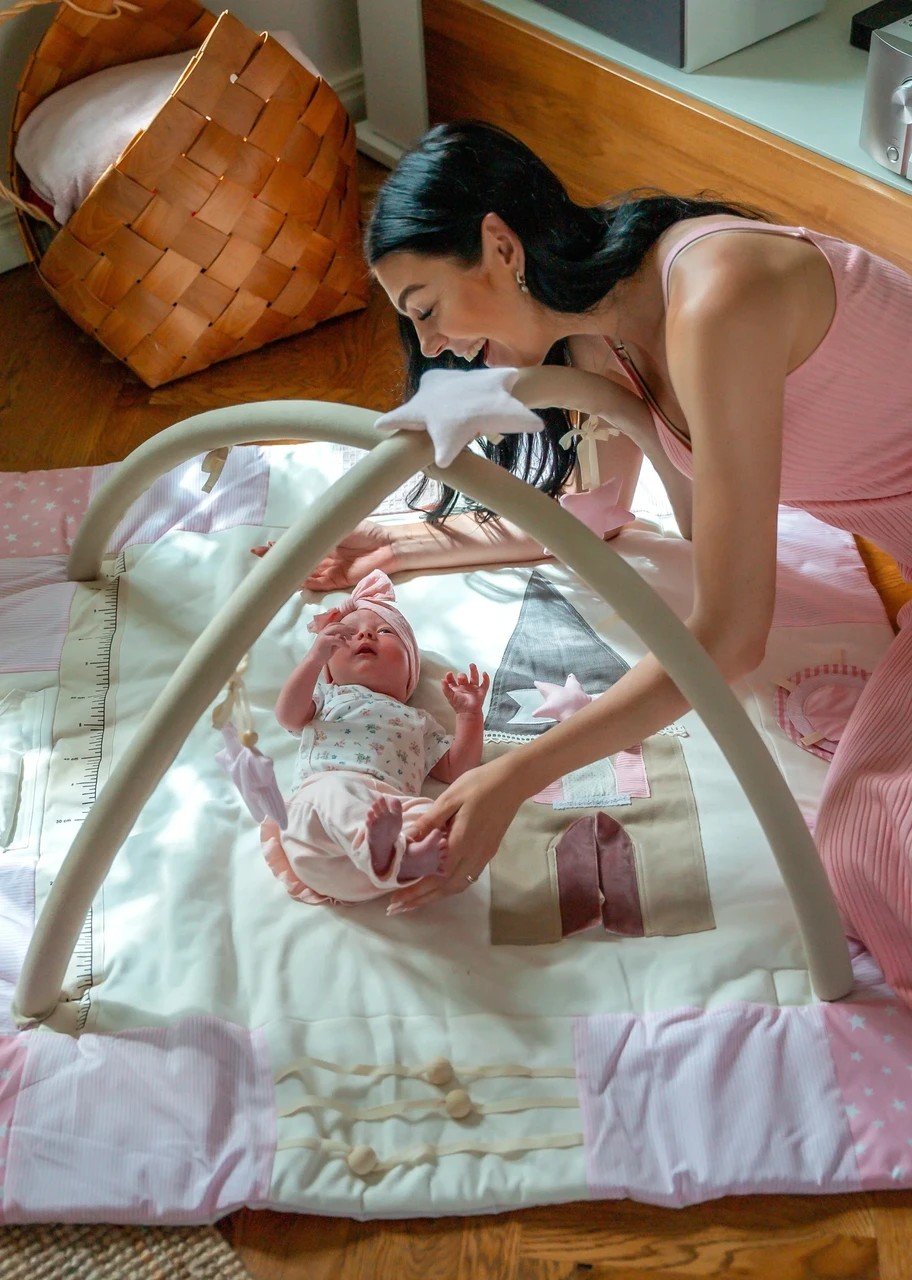 1. Woman interacting with baby on pink activity mat with arches in cozy room