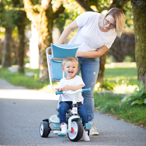 1. Woman pushing a smiling child on a blue Smoby Baby Balade Plus tricycle in a park