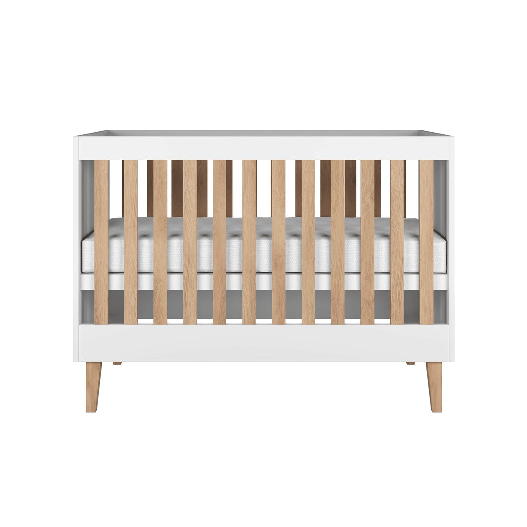 2. Front view of white baby cot with oak slats and legs in a studio setting