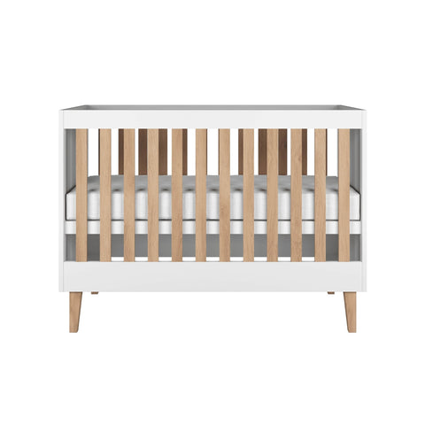 2. Front view of white baby cot with oak slats and legs in a studio setting