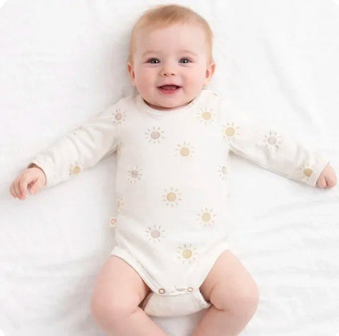 1. Smiling baby wearing Karloova sun print bodysuit lying on white bed