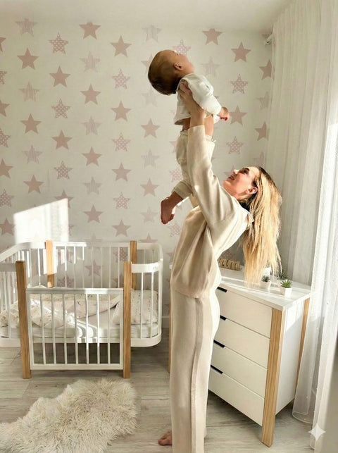 1. Woman lifting baby in nursery with KOTTO ELIN baby crib in natural and white, star-patterned wall