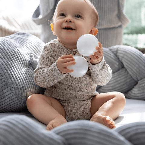 3. Close-up of infant holding white balls while sitting in grey braided baby nest by MeowBaby, highlighting soft corduroy texture