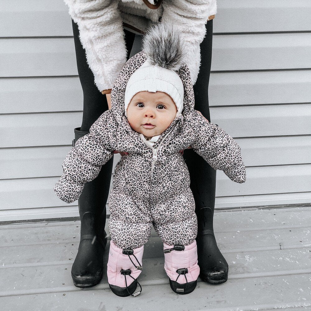 1. Baby wearing pink Stonz Puffer Booties and grey snowsuit held by adult on wooden porch
