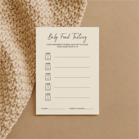 2. Single Beebila baby shower game card for baby food tasting on a beige knitted blanket, made from thick cream Munken Pure paper with spaces for guessing puree ingredients
