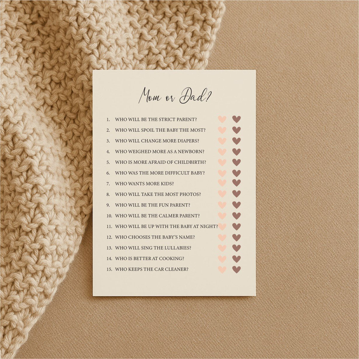 2. Single Beebila baby shower game card with 'Mom or Dad?' questions on cream Munken Pure paper, resting on a textured beige surface