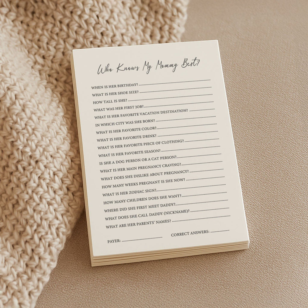 1. Stack of Beebila 'Who Knows Mommy Best' baby shower game cards on a knitted beige blanket, featuring questions about the mom-to-be's preferences and pregnancy details, printed on thick cream Munken Pure paper.
