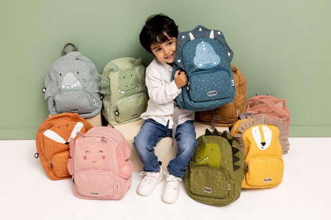1. Child holding blue dragon backpack surrounded by various colorful animal-themed backpacks