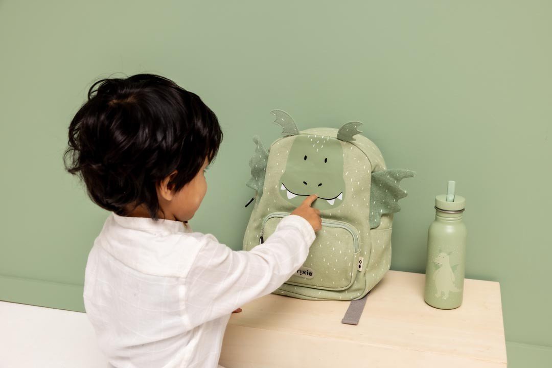 1. Child interacting with green dragon backpack next to matching water bottle, green background