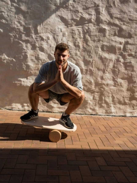 1. Man squatting on leg&go balance board with cork roller outdoors against a textured wall
