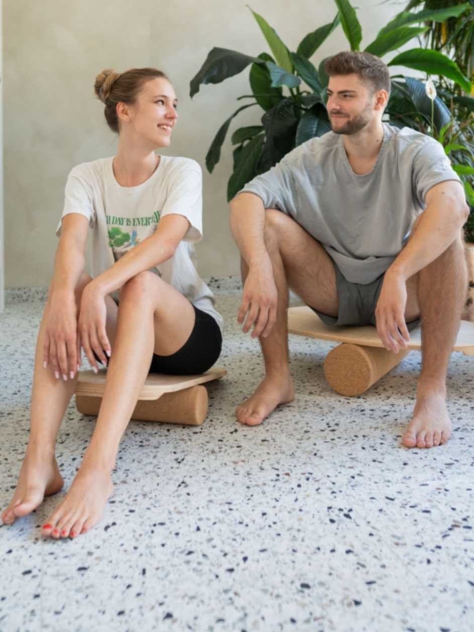 1. Man and woman sitting on round balance boards with exercise rolls on terrazzo floor, smiling at each other