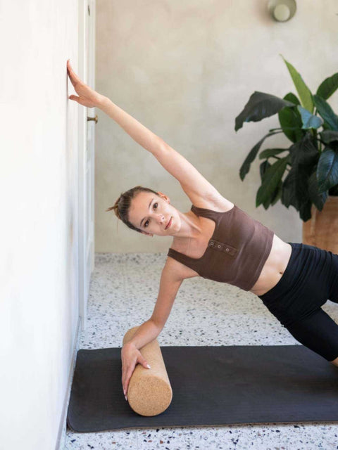1. Woman using cork roller for side stretch against wall, wearing brown top and black leggings