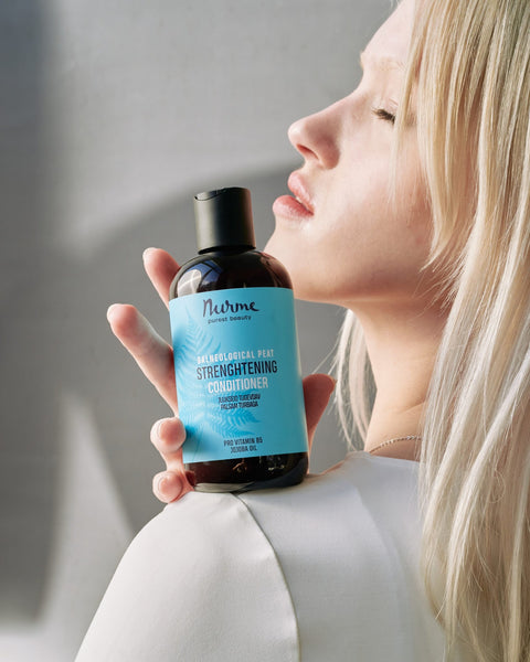1. Woman holding Nurme Balneological Peat Strengthening Conditioner bottle against her shoulder, highlighting product label and design