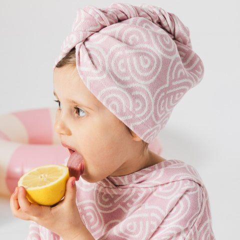 1. Child wearing pink and white patterned bamboo-cotton hair turban from Patulove, holding a lemon slice, in a playful setting