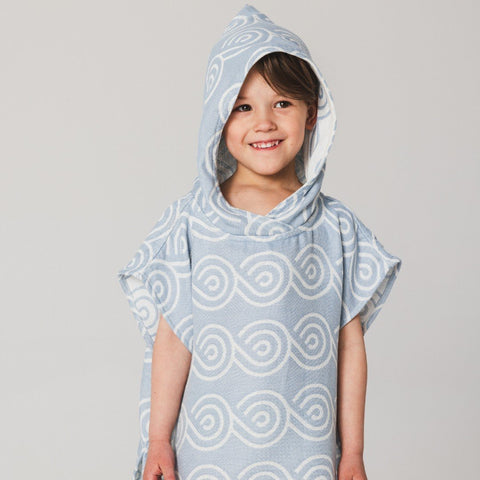 4. Child smiling in light blue Patulove bamboo bath poncho with hood and white swirl pattern, studio background