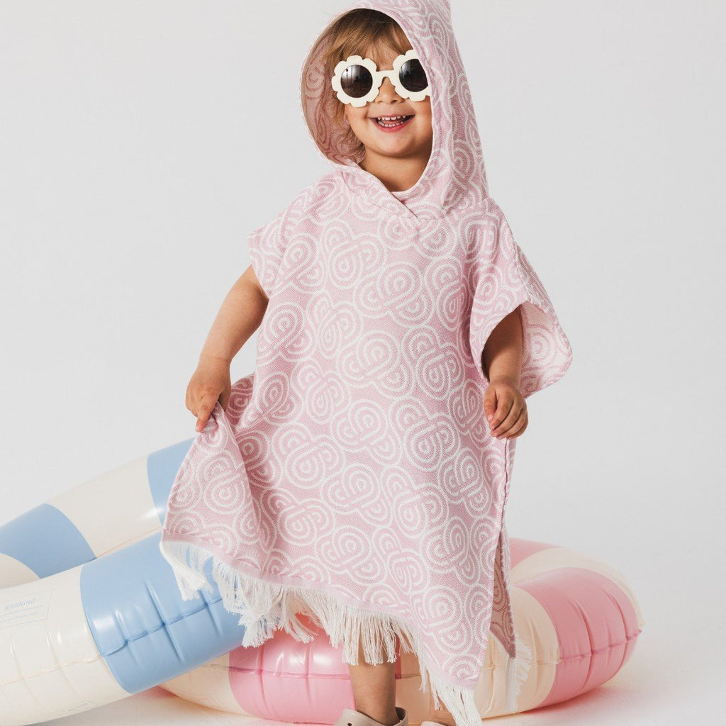 5. Child in Patulove rose bamboo bath poncho with hood, standing on inflatable pool toys, smiling