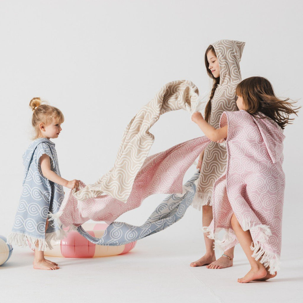 5. Three children playing in sand, blue, and pink bamboo bath ponchos with wave patterns and hoods