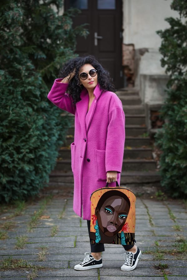 1. Woman in pink coat holding Garbanota BACKPACK SADE with unique artwork, outdoor setting