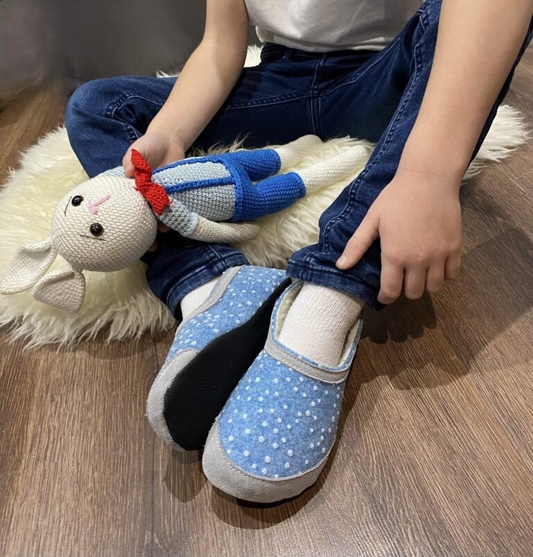 1. Child wearing blue dotted slippers sitting on wooden floor holding a toy